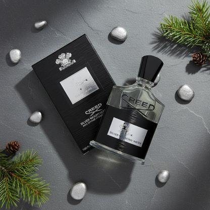 Creed Silver Mountain Water perfume bottle on grey sCreed Silver Mountain Water Eau de Parfumlate with pine branches